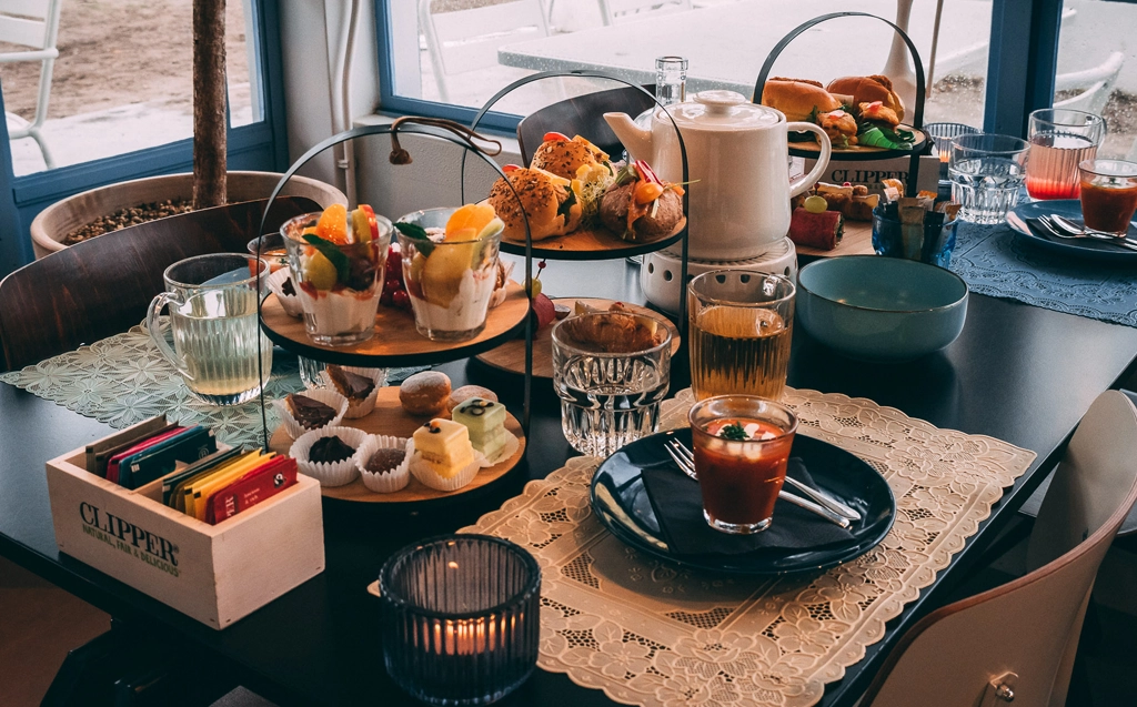 Laat je verwennen met een soepje, diverse sandwiches, mini bolletjes, mini brioche broodjes, huisgemaakte quiche, bonbons, koekjes, diverse mini petit-fours, mini brownies, huisgemaakte appeltaartkoek en een heerlijk amuseglaasje.